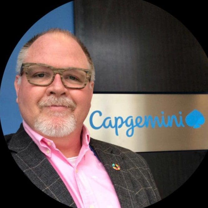 A man in glasses and a jacket standing next to a sign.