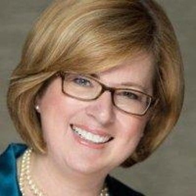 A woman with glasses and short hair wearing pearls.