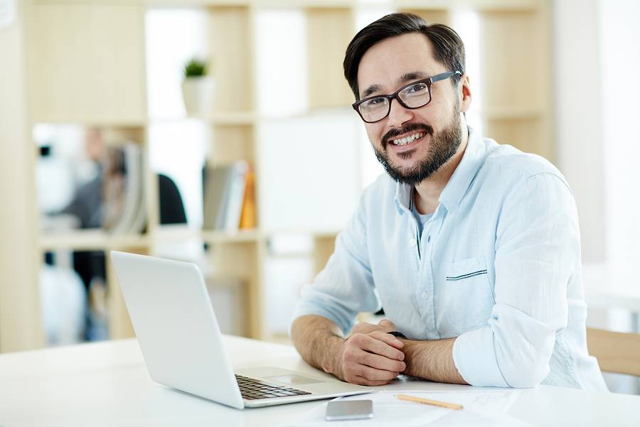 An average looking man smiling while working on the laptop