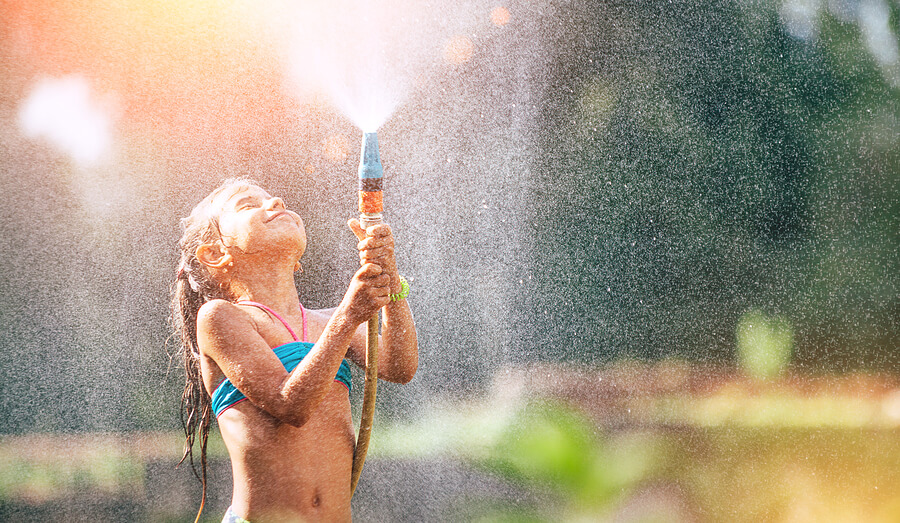 A young girl holding onto a hose and spraying water.