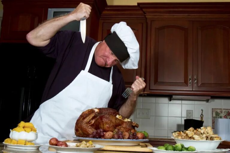 A man in chef 's hat and apron holding knife over turkey.