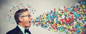A man in office attire illustrating oversharing at work with colorful letters and symbols swirling from his mouth and around his head.