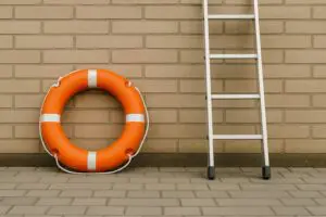 A bright orange lifesaver and a silver ladder side by side on a paved surface, symbolizing the shift from rescuer to mentor.