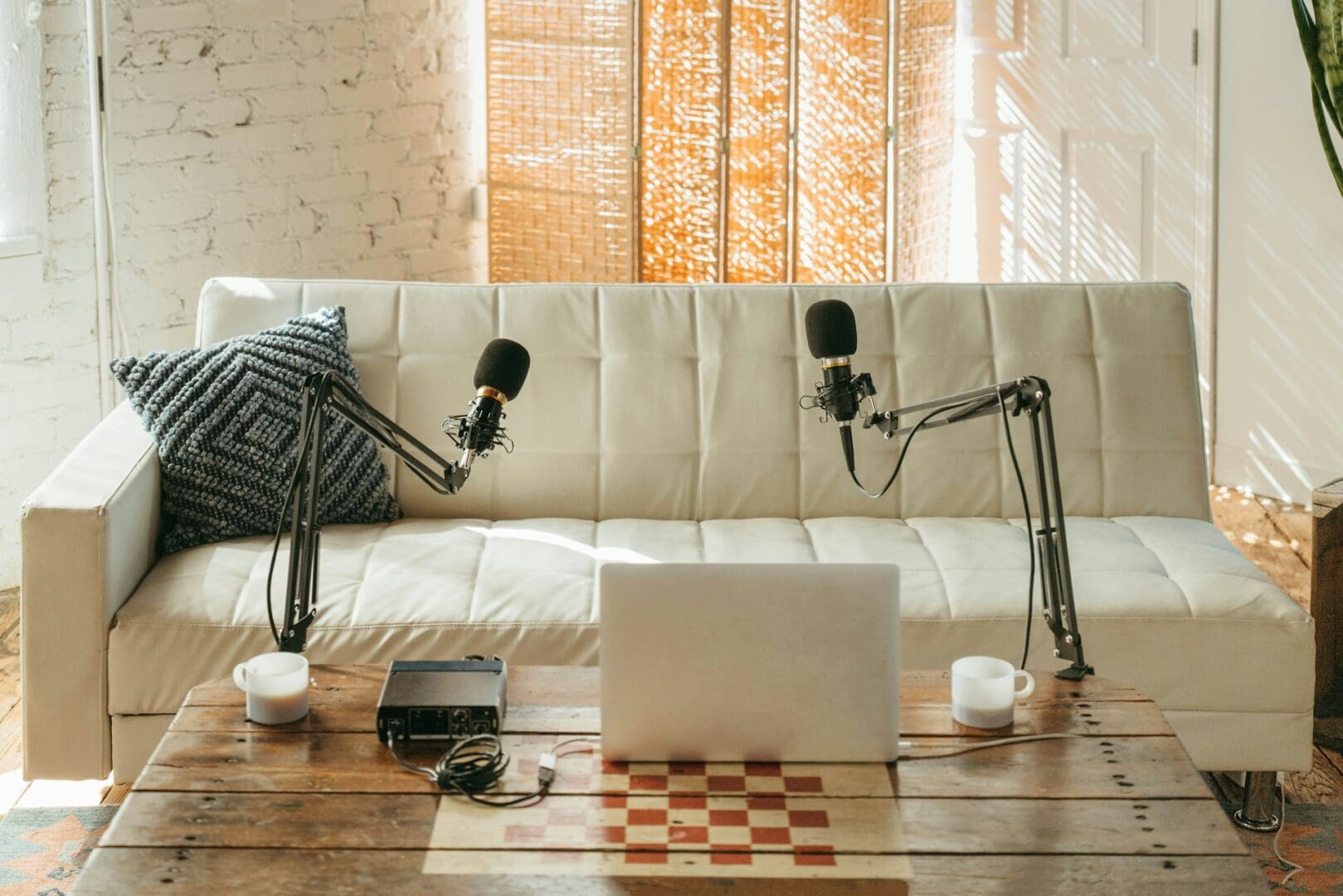 Cozy podcast setup with microphones and laptop on a glass table.